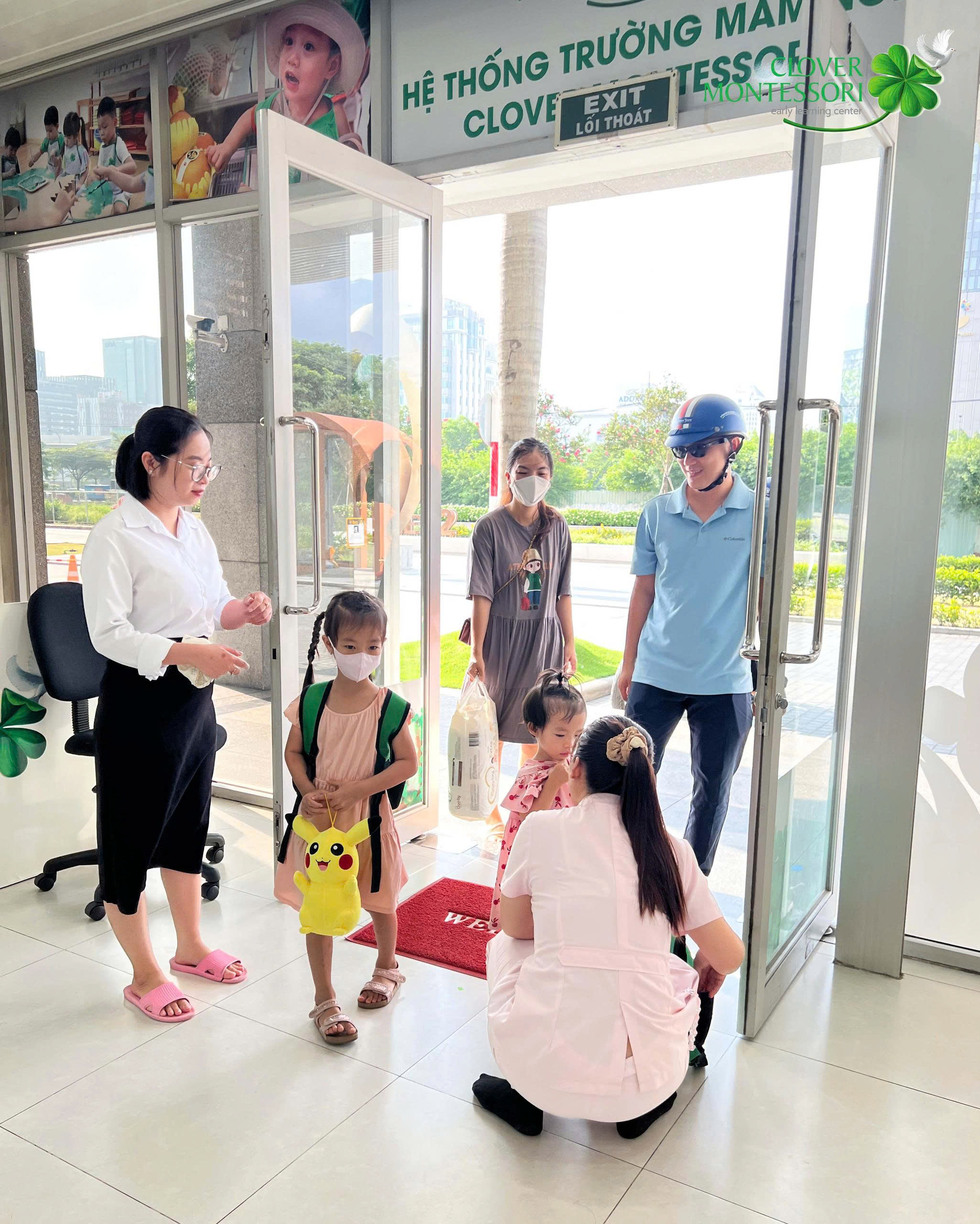 Cô giáo đón bé và phụ huynh ở cửa trường buổi sáng