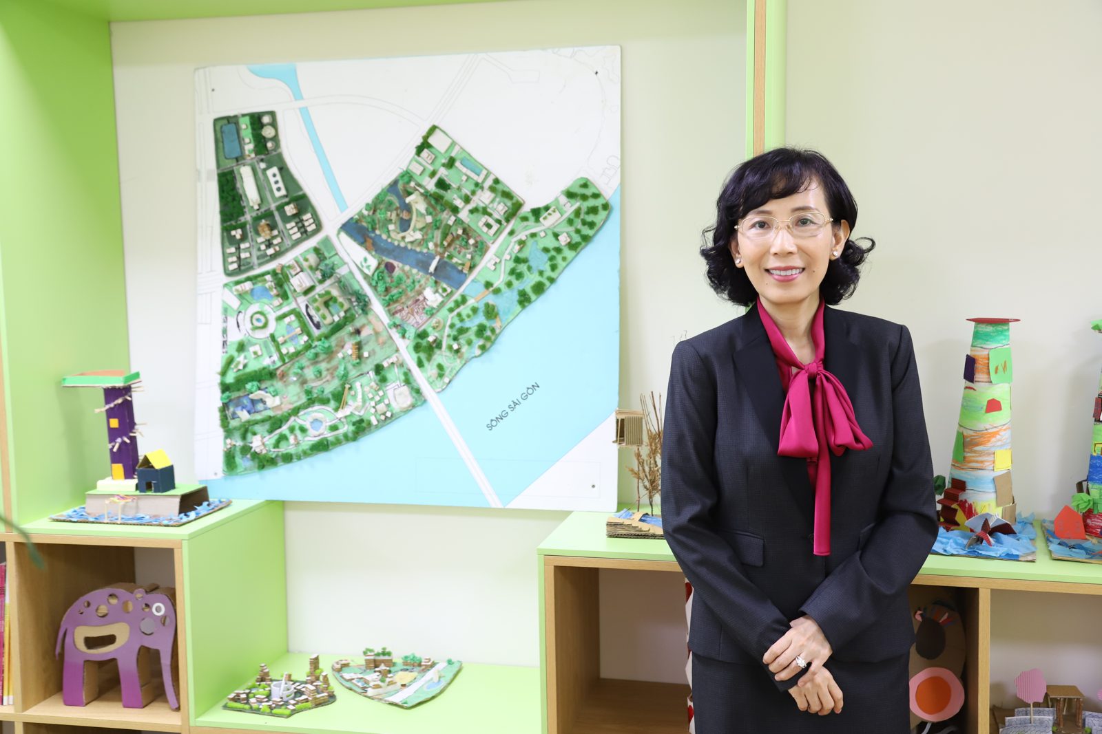 Bà giáo Trúc đứng cạnh kệ mô hình và một tấm bản đồ quy hoạch treo tường