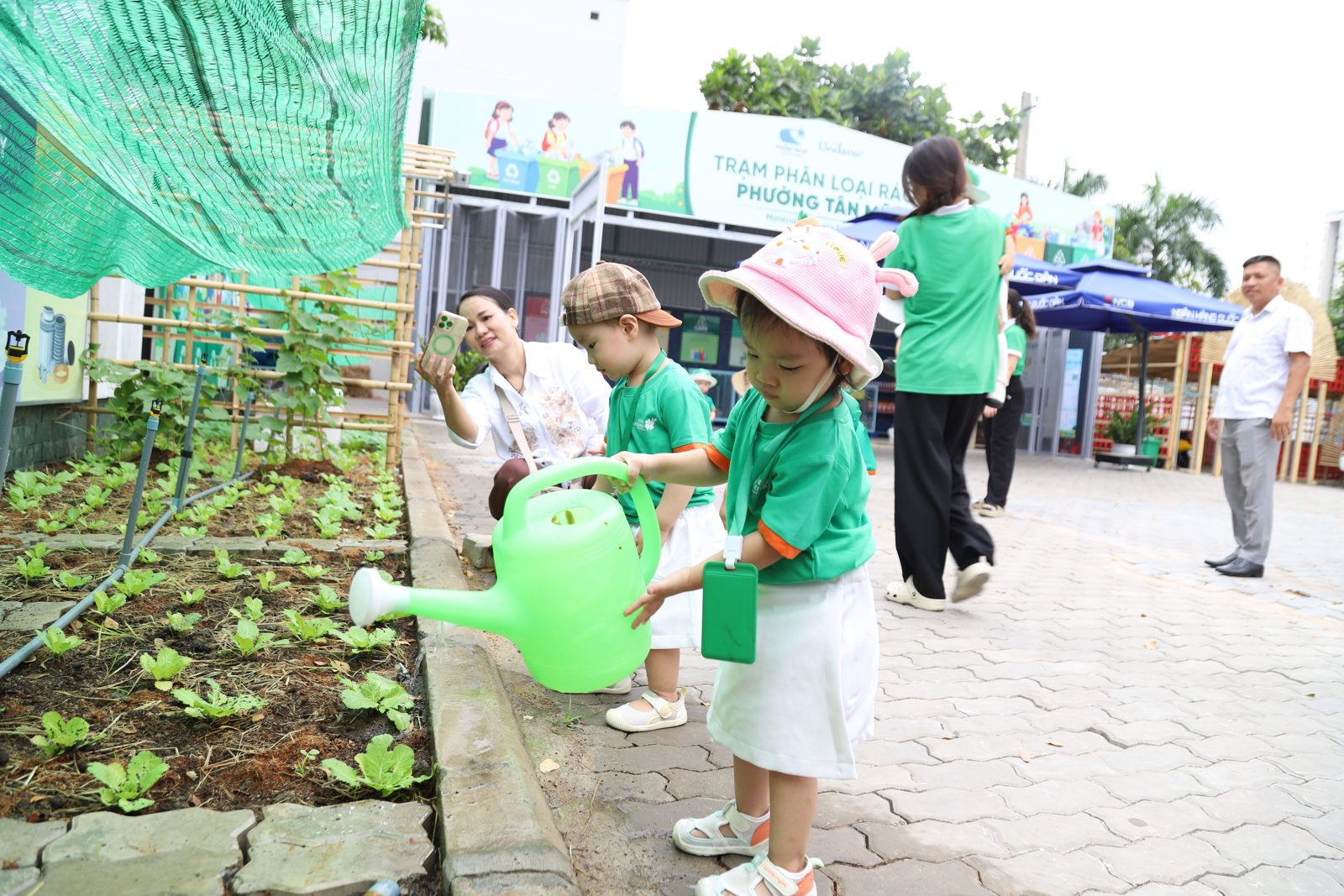 Bé tự xách bình tưới rau trong vườn
